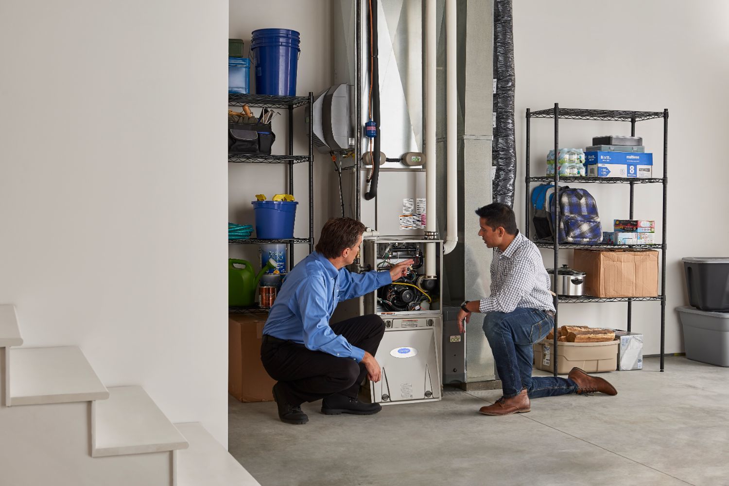 Technician and homeowner kneeling in front of a home heating system with front panel open.