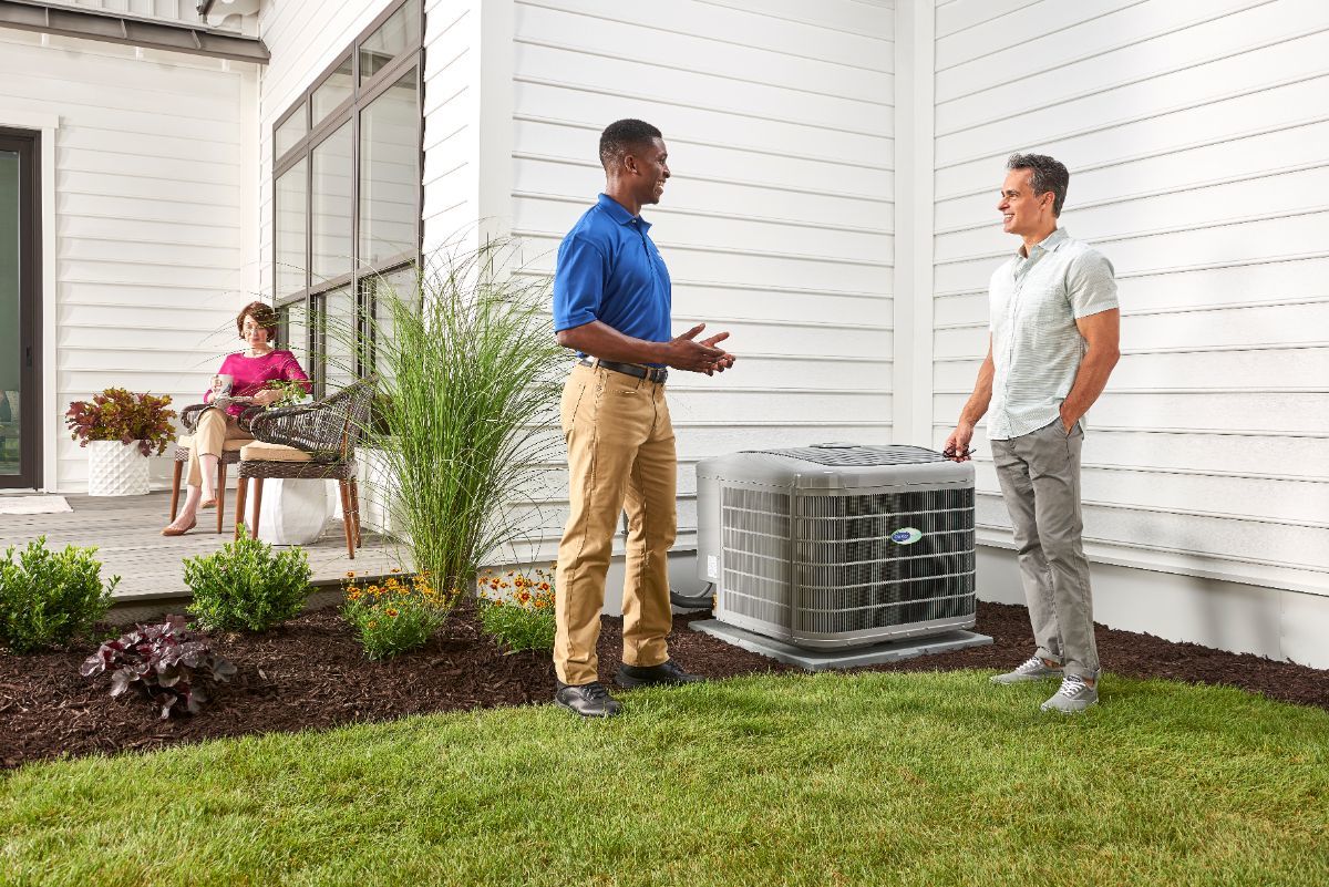 Green Air Care technician speaking with a customer outside, next to an outdoor AC unit